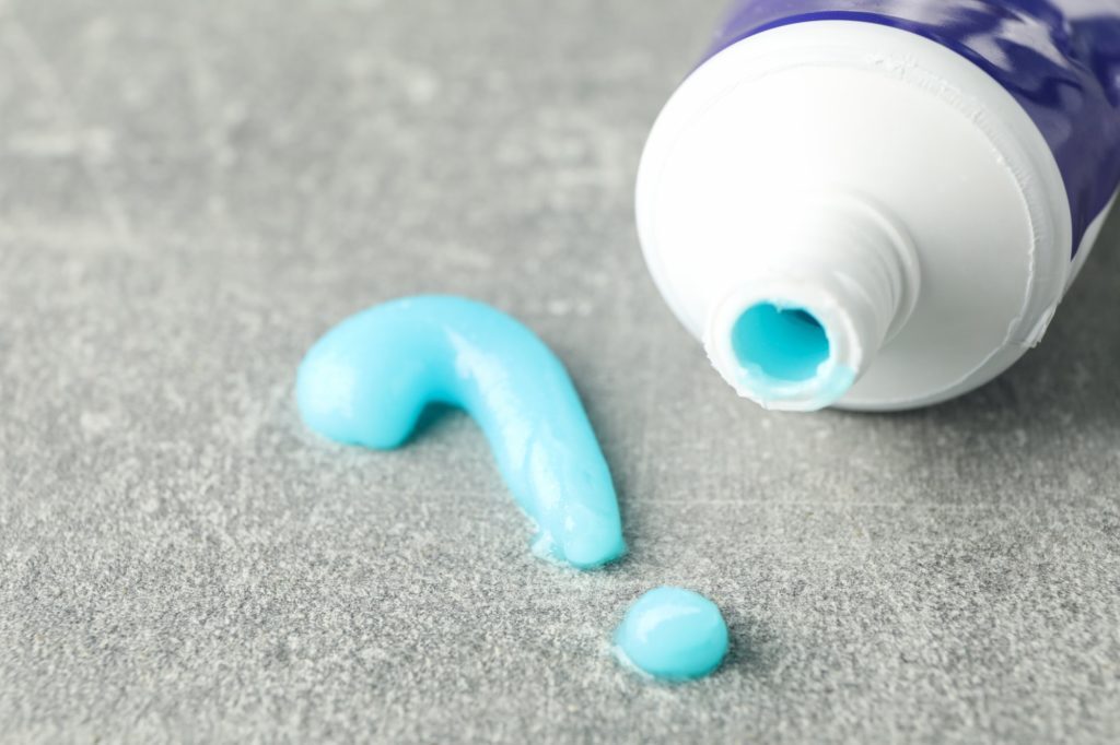 Question mark made of toothpaste and tube on gray background, closeup