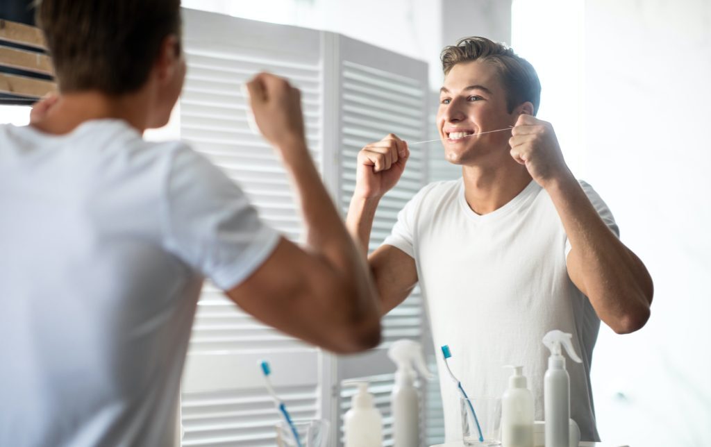 Young guy using his dental floss in bathroom