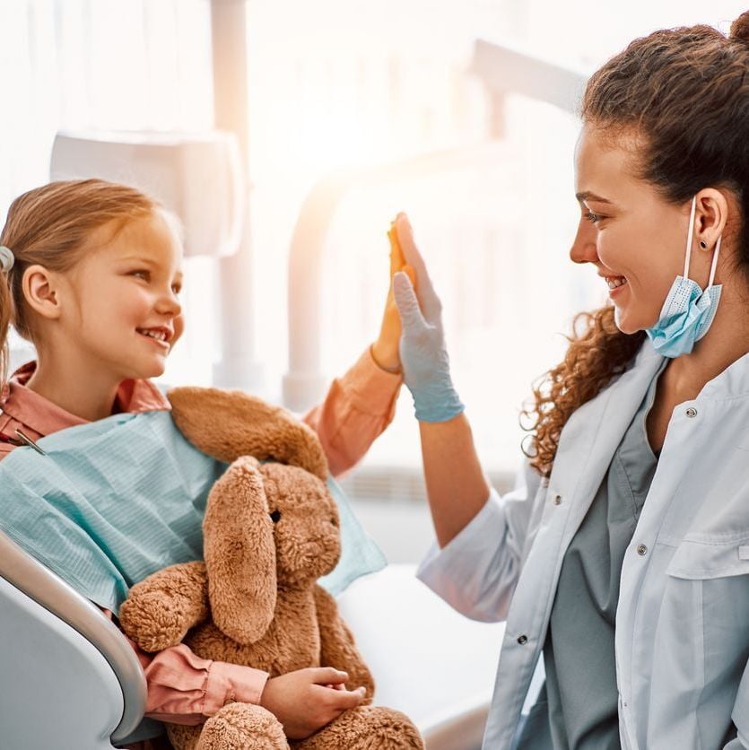 Young patient high-fiving dental staff member after appointment