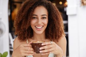 Close up portrait of young African American female model has dark healthy skin, white teeth, drinks