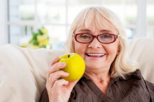 Enjoying healthy eating. Senior woman holding apple and smiling while sitting at the chair