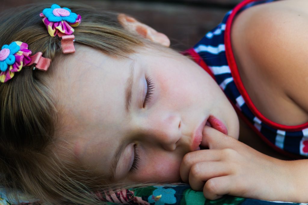 Portrait of sleeping pretty child girl who sucks her finger while sleeping.
