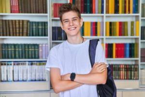 Single portrait of smiling confident male student teenager looking at camera in library